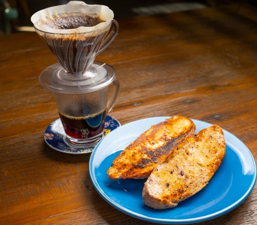 Foto do café coado da Fazenda Irarema acompanhado de um pão na chapa em um prato azul